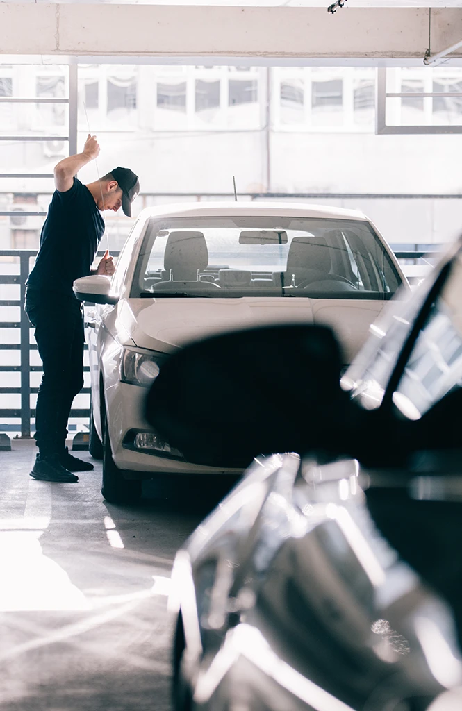 Individual inspecting a white car in a parking garage with other vehicles in view.