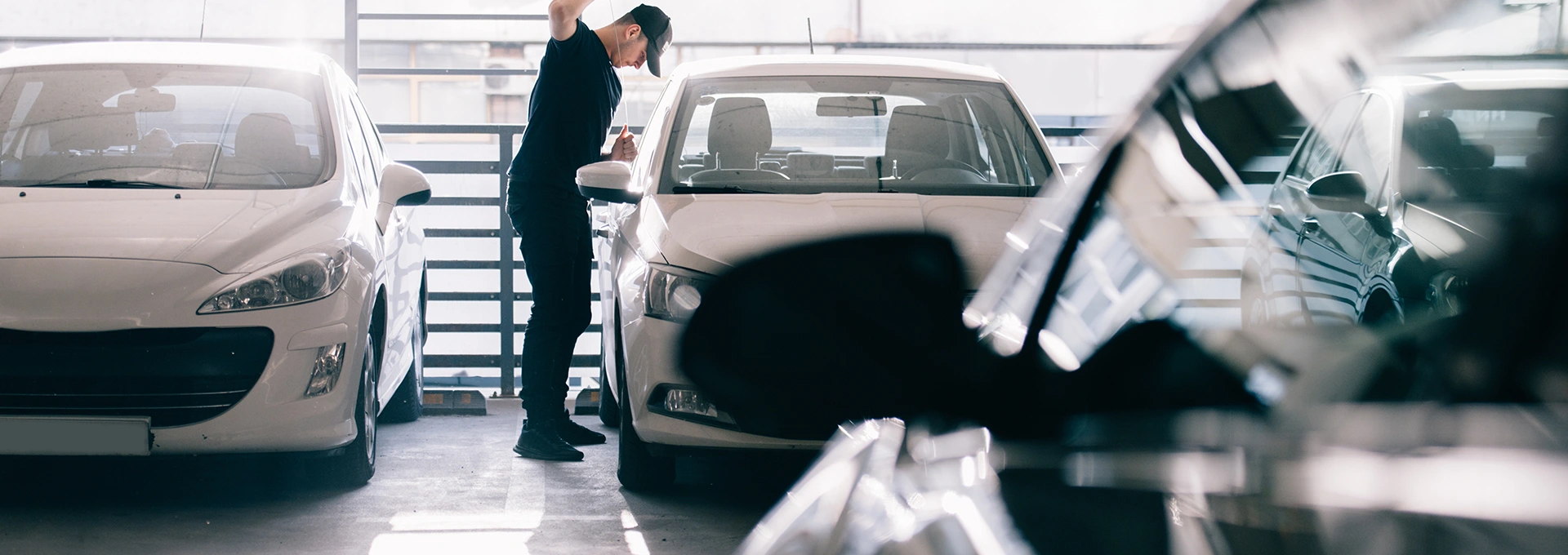 Individual inspecting a white car in a parking garage with other vehicles in view.